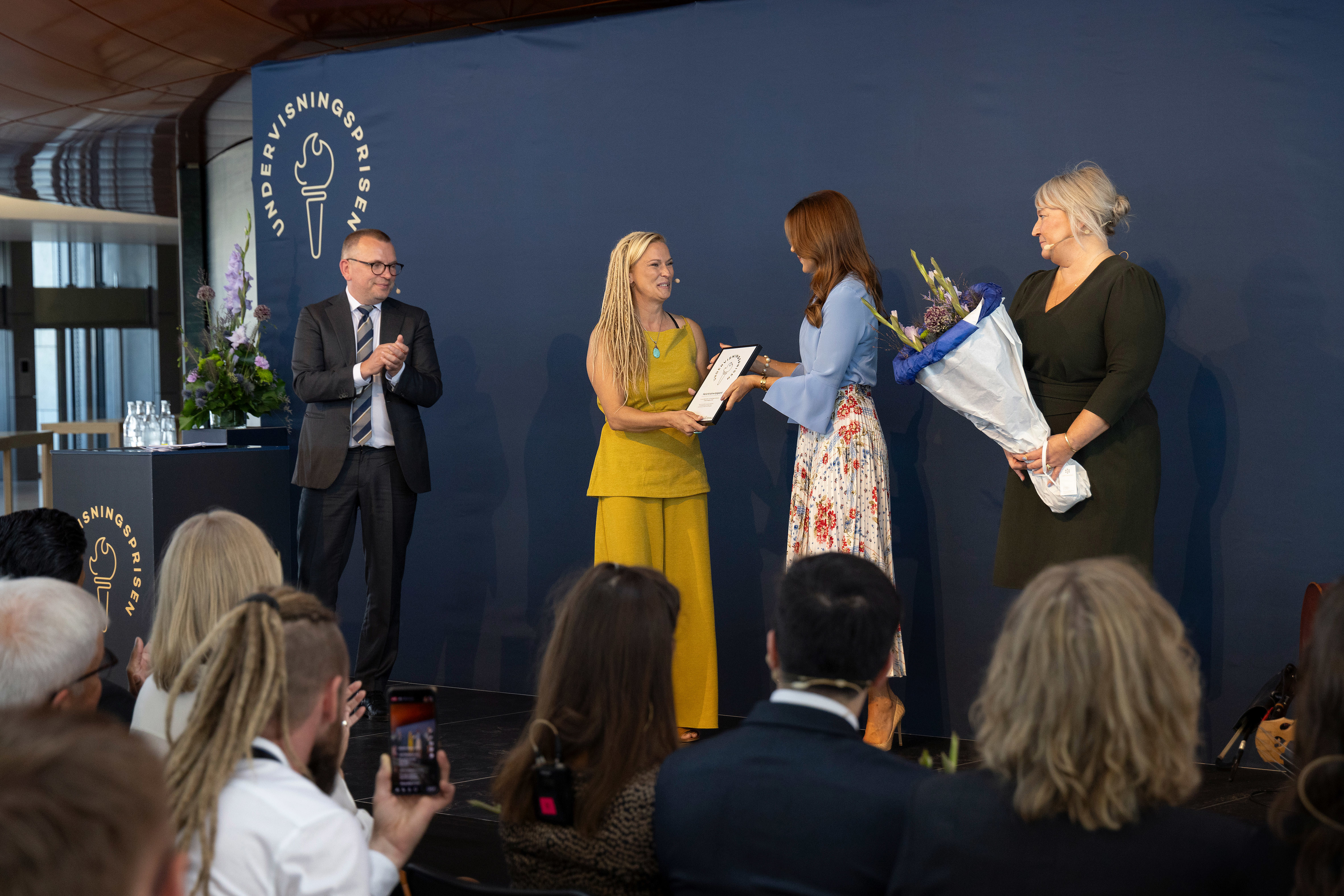Marie Kristine Kjelgaard, vinder af Undervisningsprisen 2024 får overrakt diplom og blomster af H. M. Dronningen og uddannelses- og forskningsminister Christina Egelund.