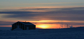 Foto af solnedgang med en hytte i forgrunden.
